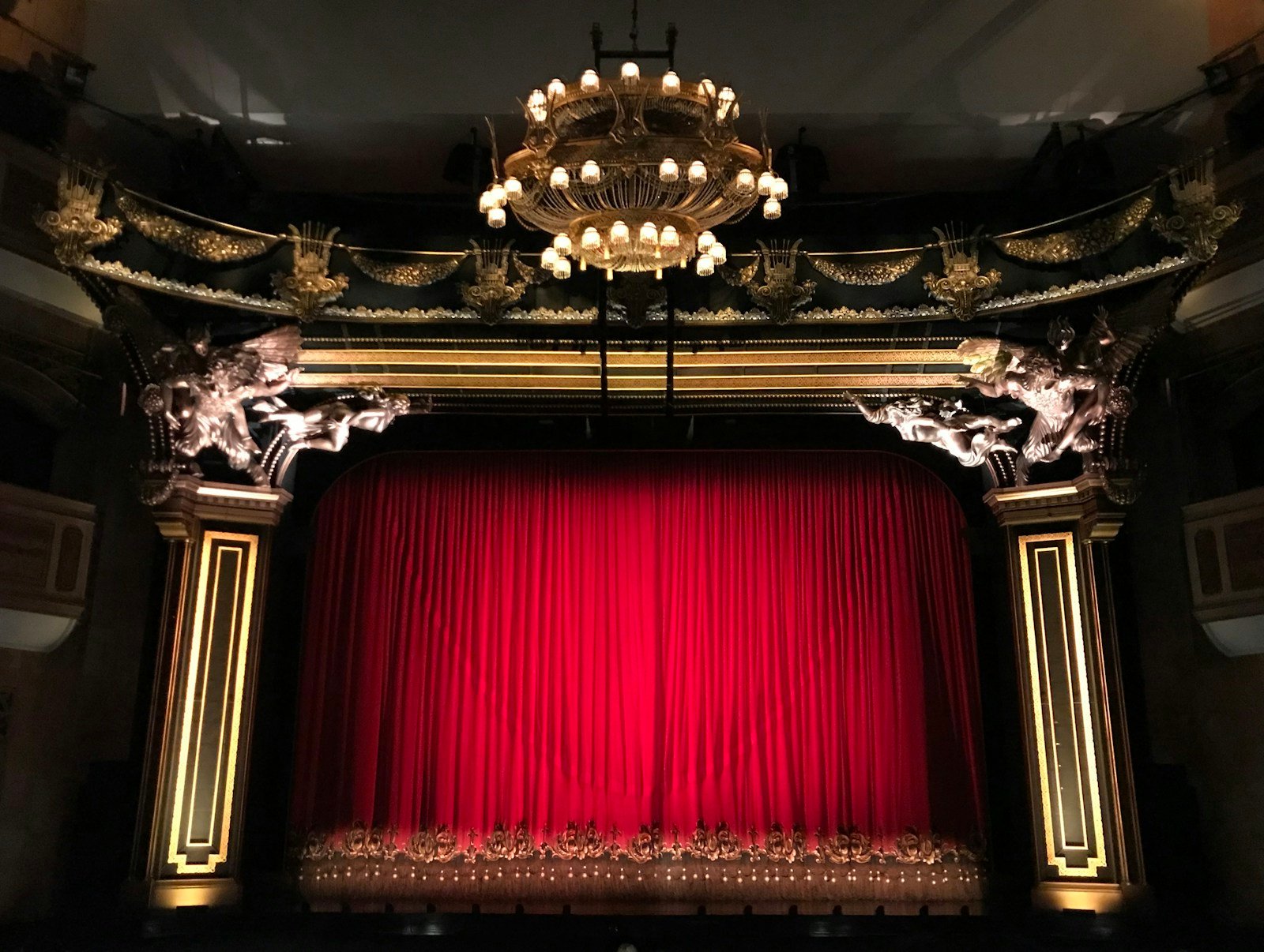 Iliustracinė teatro salės nuotrauka su raudona uždanga.